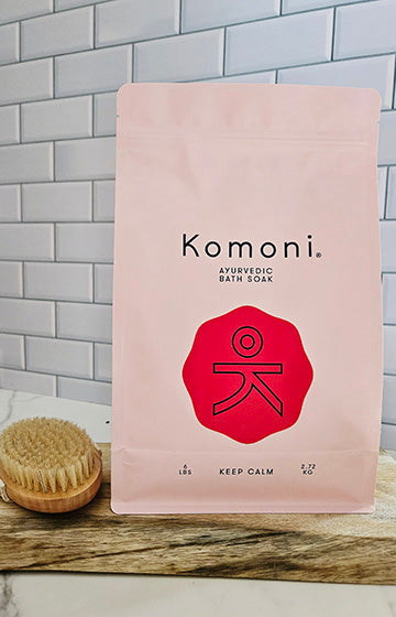 Komoni Ayurvedic bath soak 6 pound package with a red logo on a gray tiled wall background