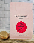 Komoni Ayurvedic bath soak 6 pound package with a red logo on a gray tiled wall background