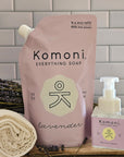 Komoni Everything Soap refill packaging with lavender scent on a wooden surface with a tiled wall background.