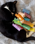 A black cat with white patches shown curled up with all the colorful boxes of Komoni's pure essential oils.