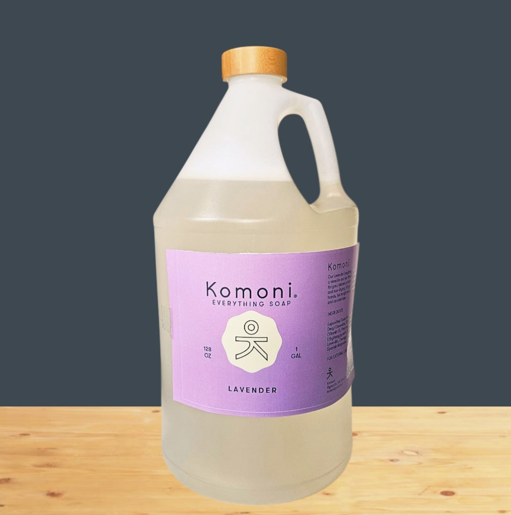 Komoni lavender soap 1 gallon bottle with bamboo wood cap on a wooden surface with a dark gray background