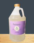 Komoni lavender soap 1 gallon bottle with bamboo wood cap on a wooden surface with a dark gray background