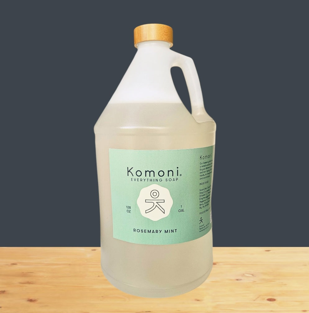 Gallon bottle of Komoni Everything Soap  with a bamboo wood cap on a wooden surface with a dark gray background