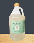 Gallon bottle of Komoni Everything Soap  with a bamboo wood cap on a wooden surface with a dark gray background