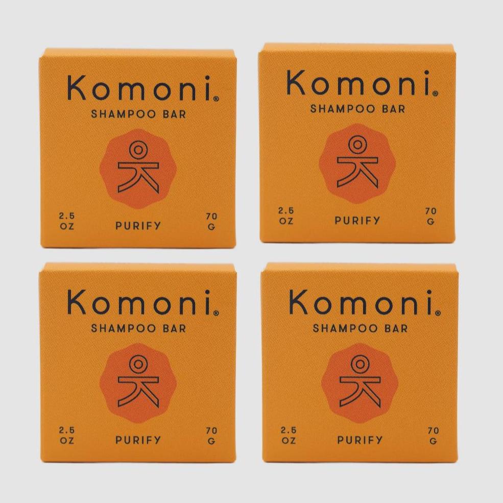 Four orange boxes of Komoni eco-friendly, concentrated PURIFY Essential Oil Shampoo bars shown in a grid.