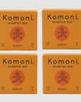 Four orange boxes of Komoni eco-friendly, concentrated PURIFY Essential Oil Shampoo bars shown in a grid.