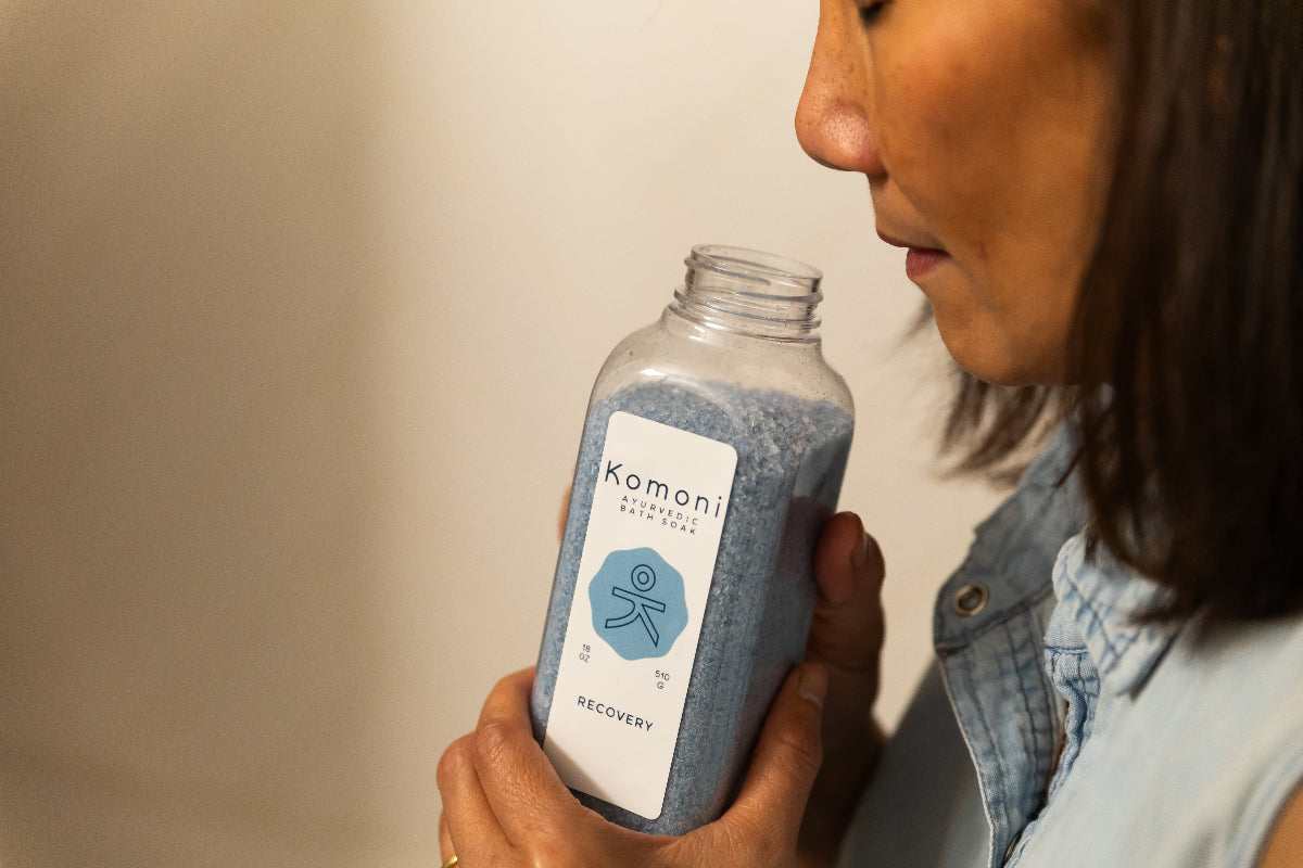 Komoni founder holding and smelling an open bottle of RECOVERY Bath Soak with a neutral background
