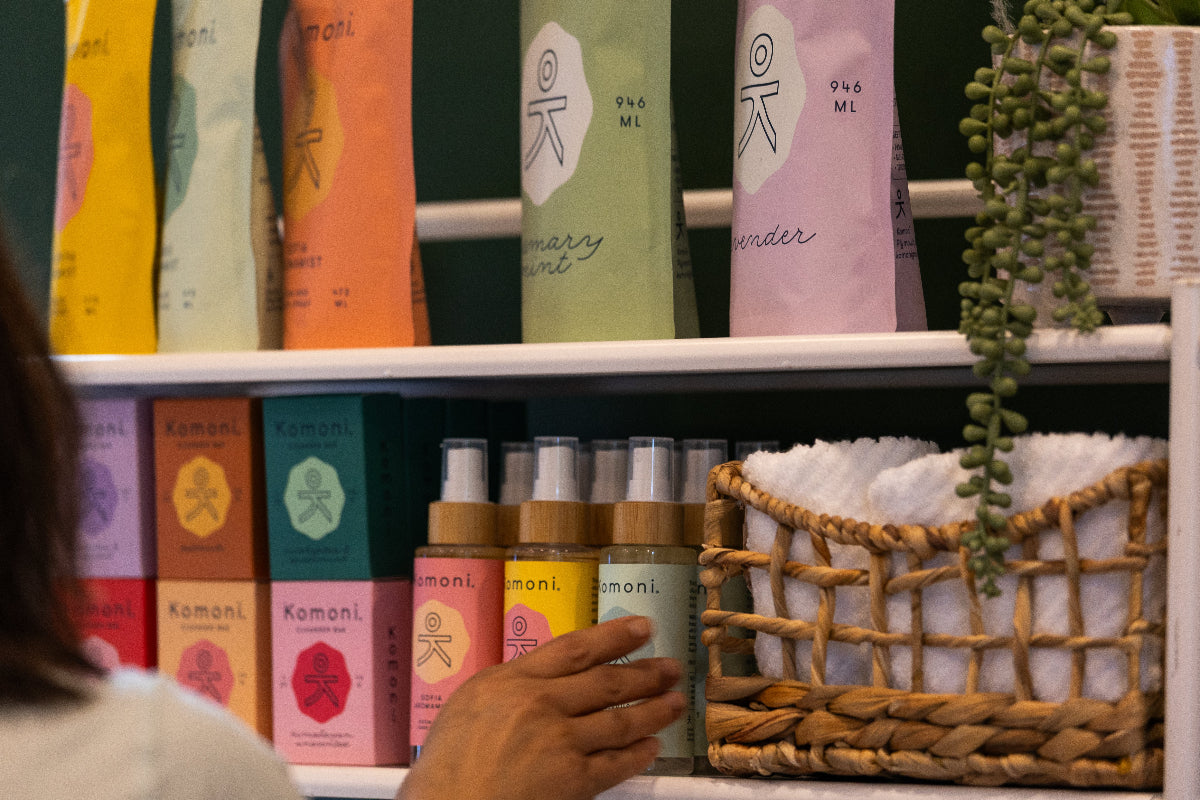 Shelf with various colorful Komoni products including eco-friendly product refill pouches, with a person partially visible.