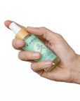 A hand shown holding a spray 2 oz. bottle of Four Thieves E3 rated moisturizing hand sanitizer.