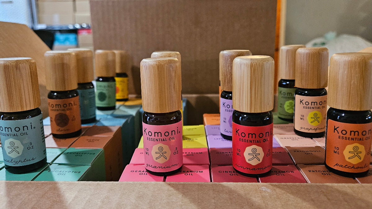 Collection of Komoni Pure Essential Oil 10 mL vials with bamboo wood tops on a table with a blurred background.