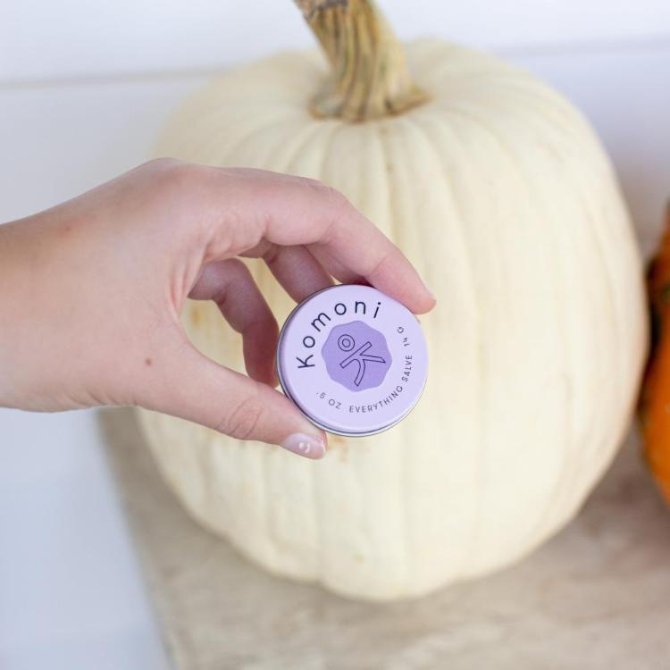 A close-up of a hand holding a tin of Lavender purple pocket sized tin of SOOTHE Everything salve.